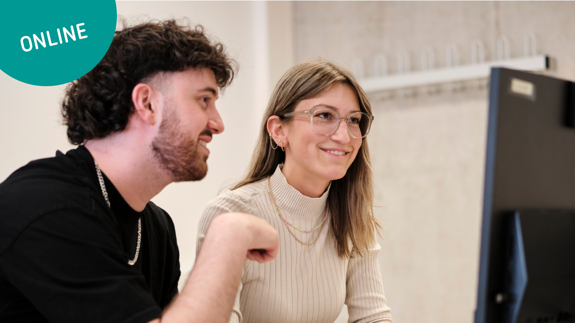 Zwei Studierende blicken auf einen Computer-Bildschirm und unterhalten sich