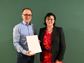 Ein Mann steht mit einer Frau vor einer grünen Wand. 
