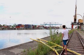 Ein junger Mann steht mit dem Rücken zur Kamera auf Schienen im Straßburger Hafen am Rhein.