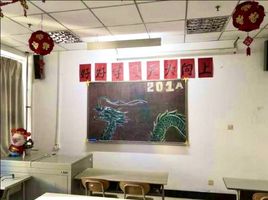 Ein kleines Klassenzimmer an der Qingdao Universität. Eine dunkelgrüne Tafel mit einem aus Kreide gemaltem Drachen hängt an der weißen Wand, welche mit roten, chinesischen Dekorationselementen geschmückt ist. 