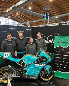 Das Bild zeigt das türkisfarbene E-Motorrad Amperia 23 am Messestand. Dahinter stehen vier Teammitglieder von eLaketric in dunklen Kapuzenpullovern und lächeln stolz in die Kamera.