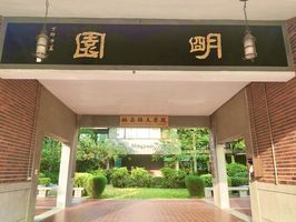 Eine kleine Unterführung, auf der oben in goldenen chinesischen Zeichen auf schwarzem Stein "Mingyuan" steht, führt zu einem kleinen Gartenbereich vor dem Campus of European and Asian Languages der Wenzao Ursuline University in Taiwan. 