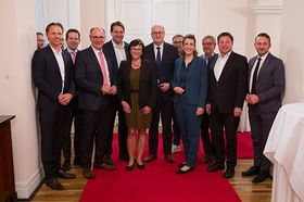 Gruppe von Personen auf einem roten Teppich vor einer weißen Wand