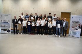 Eine Gruppe Studierender und zwei ältere Männer stehen zusammen und lächeln zufrieden