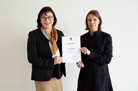 Das Foto zeigt Prof. Dr. Sabine Rein (links) und Prof. Dr. Sarah Hanisch (rechts). Sie halten gemeinsame die Ernennungsurkunde in der Hand.