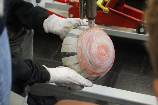 Blick auf eine Schüssel, die von zwei Händen in Handschuhen gehalten wird. Aus einer Maschine tropft flüssiger Kunststoff auf die Schüssel.