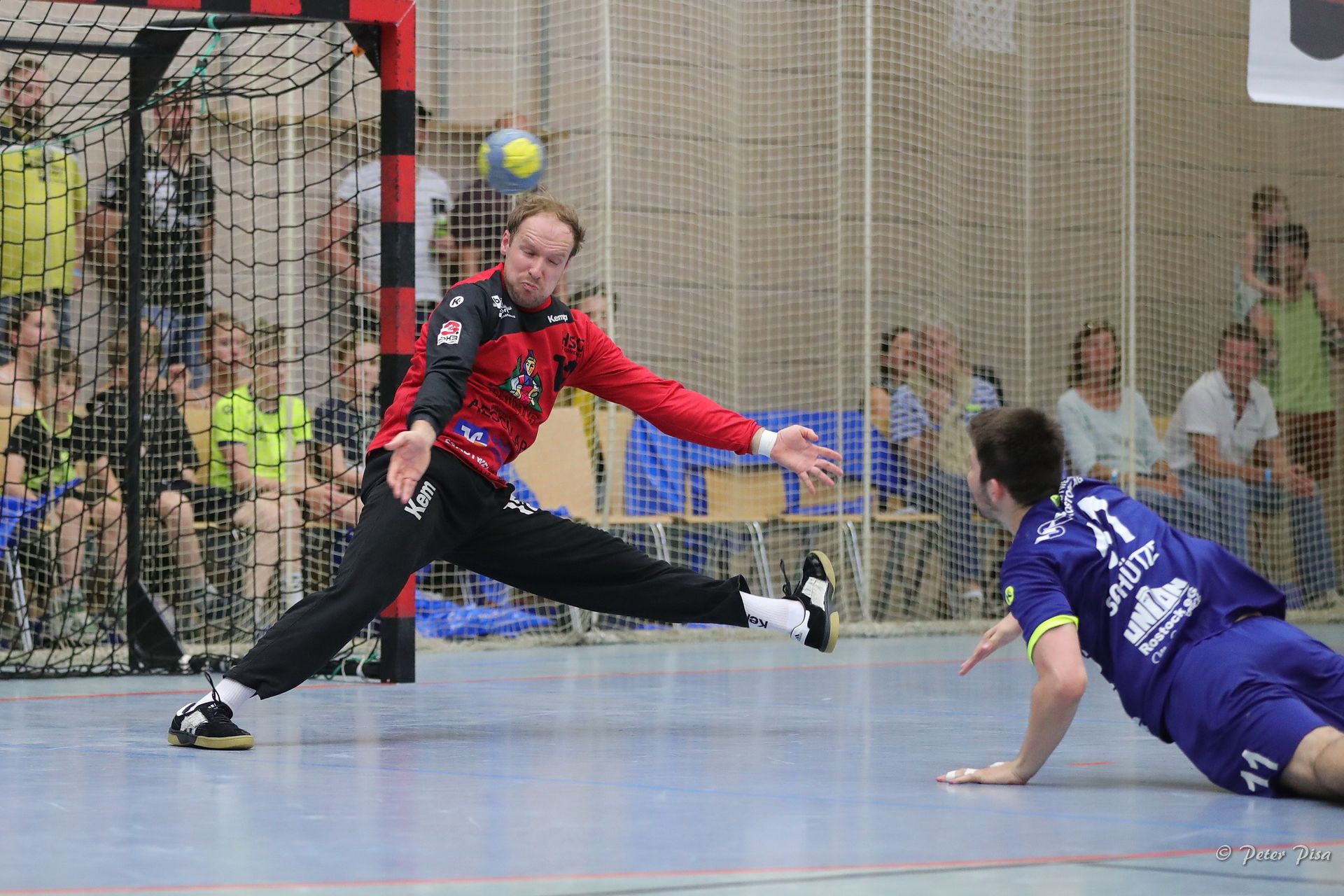 Simon Tölke in Aktion vor dem Tor beim Versuch den Angriff eines Gegners abzuwehren. Der gegnerische Spieler fängt sich nach seinem Wurf mit der linken Hand auf dem Boden ab. Der Ball fliegt auf Simon Tölke zu.