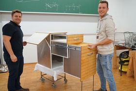 Alexander Steiner (links) und Janik Fleischhut (rechts) stehen neben ihrem Einbauschrank, bei dem Schubladen nach vorne ausgezogen sind.