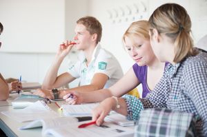 Drei Studierende sitzen in einer Vorlesung und besprechen eine Aufgabe.