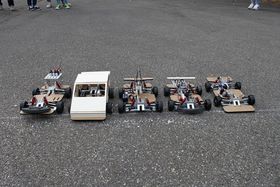 Blick aus der Vogelperspektive auf fünf Modellautos, die in einer Reihe auf Asphalt nebeneinander stehen.