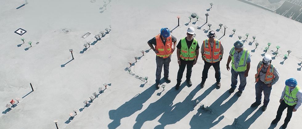 Luftaufnahme von sechs Menschen mit Schutzhelmen und Warnwesten auf einer Baustelle.