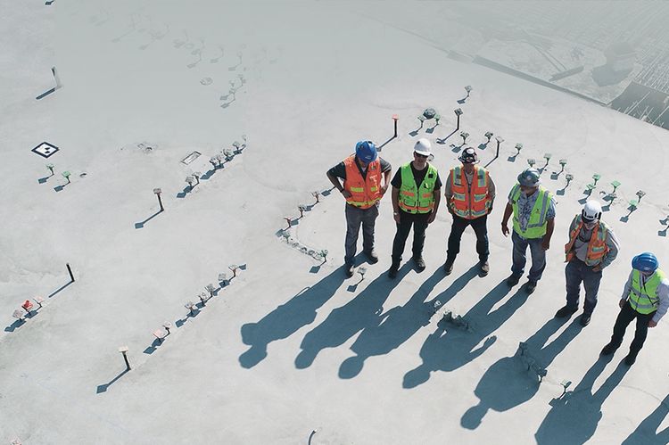 Luftaufnahme von sechs Menschen mit Schutzhelmen und Warnwesten auf einer Baustelle.