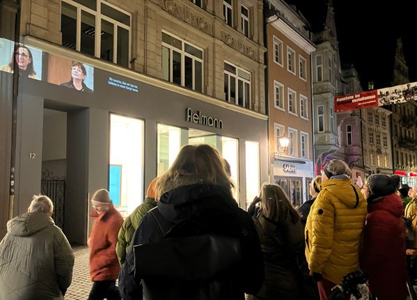 Eine Menschengruppe steht im Dunkeln und blickt auf eine Häuserfassade, auf die ein Film projiziert wird.