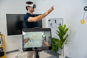 Ein Mann trägt eine VR-Brille und steht in einem Büro mit zwei Bildschirmen