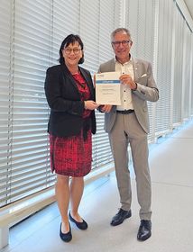 Das Bild zeigt Prof. Wolfmaier und Prof. Rein in einem grauen Gang. Sie halten gemeinsam die Urkunde zum Beitritt der HTWG in die HfSW