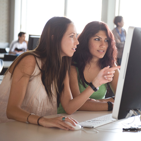 Zwei Studentinnen schauen gemeinsam auf einen PC-Bildschirm im Vorlesungssaal.