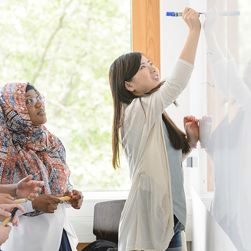 Asiatisch aussehende Studentin schreibt vor Studierenden unterschiedlicher Herkunft auf Whiteboard