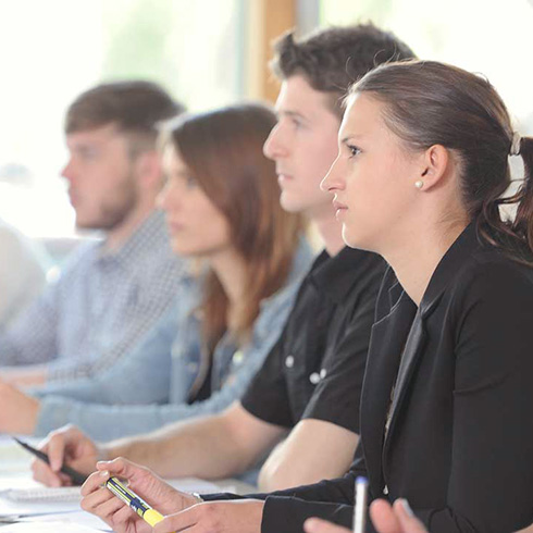 Vier Studierende sitzen nebeneinander in einem Vorlesungsraum und blicken in die gleiche Richtung. 