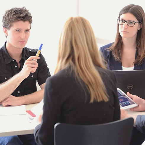 Drei Studierende diskutieren an einem Tisch.