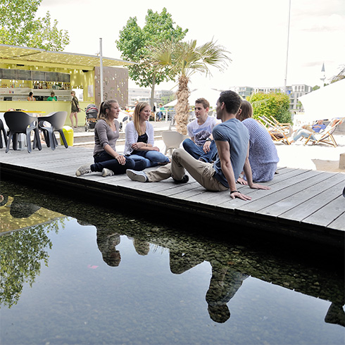 Five students are having a conversation while sitting on the walkway of the beach bar