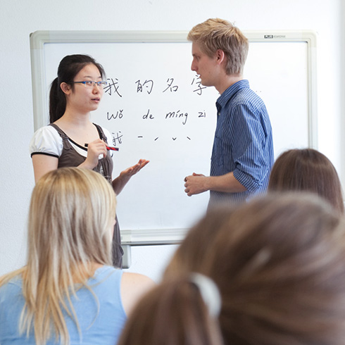 Studentin und Student unterhalten sich vor Tafel mit chinesischen Schriftzeichen