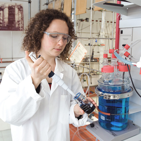 Studentin spritzt im Chemie-Labor mit großer Spritze Flüssigkeit in einen Messbecher