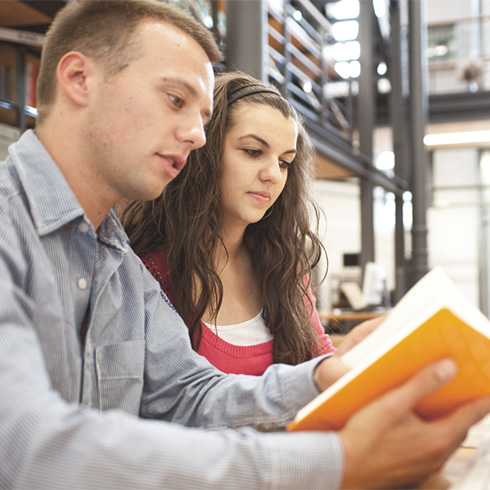 Student und Studentin lesen in der Bibliothekshalle gemeinsam in einem Buch