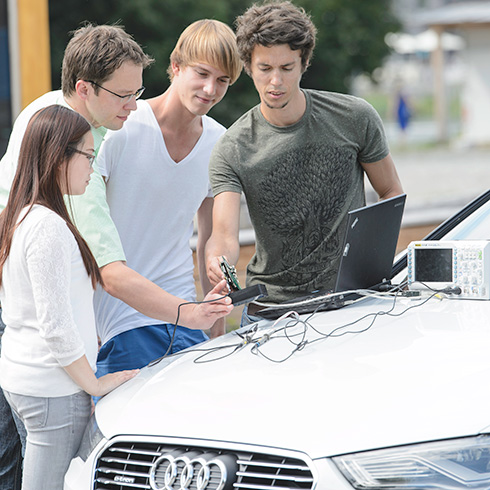 Professor und drei Studierende führen Messungen an einem Fahrzeug durch