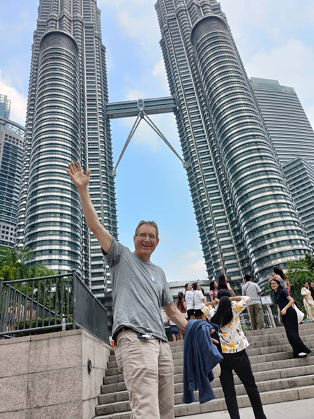Ein Mann steht winkend vor den Petrona Towers in KL