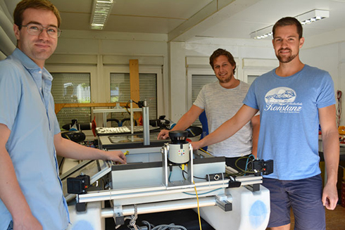 Gruppenbild, von links: Patrick Hoher, Tim Baur und Julian Böhler stehen in einer Garage um den Wasserroboters CaRoLime (Catamaran Robot Locomotion In Maritime)