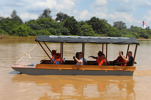 Ein Boot auf einem sehr lehmigen Fluss. Das Boot hat ein aufgeständertes Dach, im Boot sitzen acht Personen mit leuchtend roten Rettungswesten.