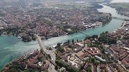 Stadtansicht von oben. Ein Fluss teilt die Stadt in zwei Bereiche, die durch mehrere Brücken verbunden sind.