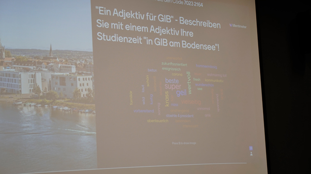 Projektionsfläche, auf der links Gebäude an einem Fluss zu sehen sind und rechts eine Wortwolke mit Begriffen zu der Frage "Ein Adjektiv für GIB - Beschreiben Sie mit einem Adjektiv Ihre Studienzeit in GIB am Bodensee!" 
