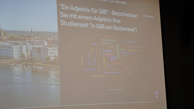 Projektionsfläche, auf der links Gebäude an einem Fluss zu sehen sind und rechts eine Wortwolke mit Begriffen zu der Frage "Ein Adjektiv für GIB - Beschreiben Sie mit einem Adjektiv Ihre Studienzeit in GIB am Bodensee!"