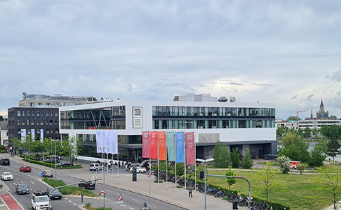 Ein großes Gebäude vor dem Fahnen wehen, davor eine Straße.