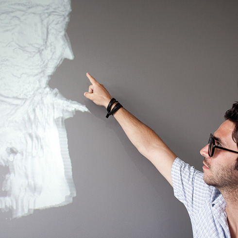 rechts steht eine Person vor einer Leinwand, die mit ausgestrecktem Arm auf eine 3D-Visualisierung links auf der Leinwand zeigt