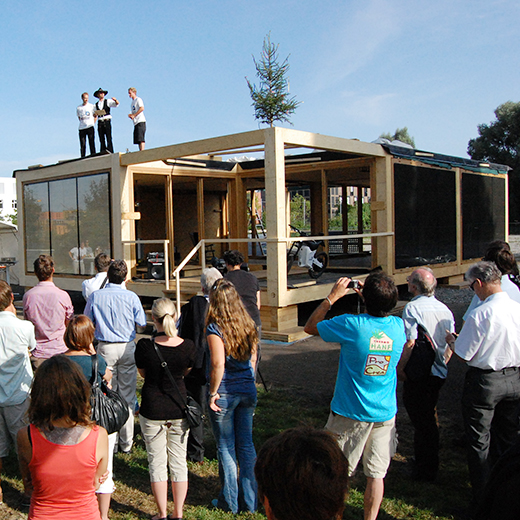 Richtfest Solarhaus ecolar: Personen betrachten Zimmermann auf Dach des Gebäudes