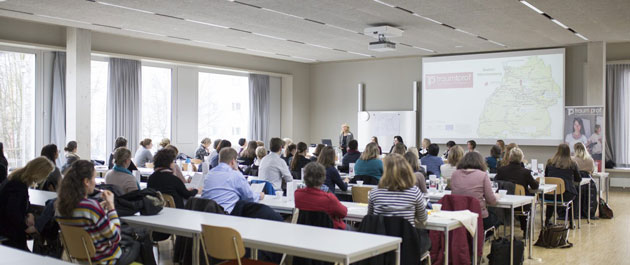 Ein voll besetzter Seminarraum von hinten fotografiert. An die Wand ganz vorne ist eine Präsentationsfolie mit einer Karte projeziert.