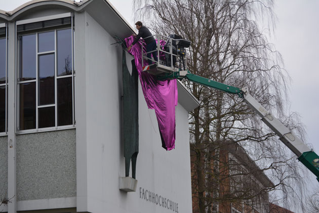 Die HTWG-Aula von außen: Zwei Männer im Korb eines Teleskopmastes verhüllen die an der Wand angebrachte Prometheus-Statue mit einem großen Tuch.