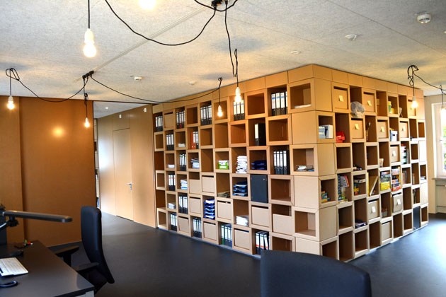 Ein Büroraum mit einem großen Regal voller quadratischer Fächer mit Ordnern und Büchern.