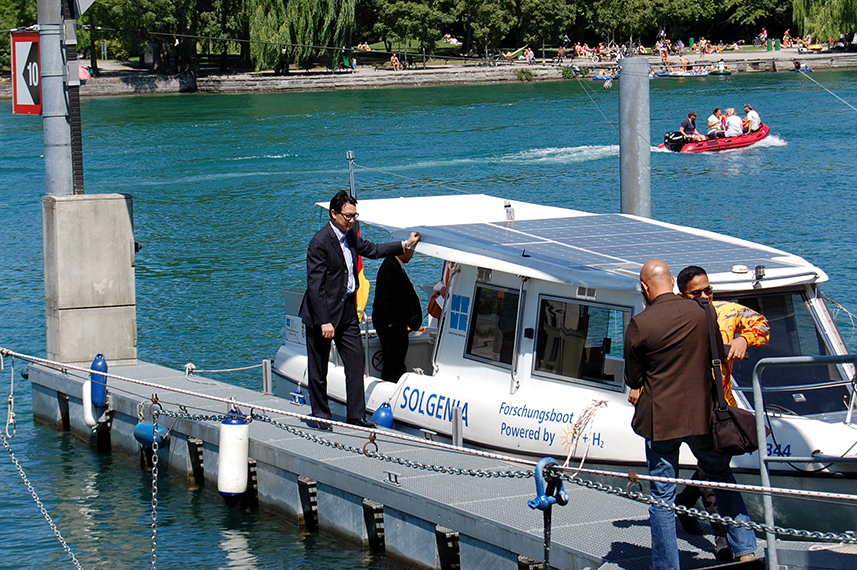 Das Forchungsboot Solgenia der HTWG ankert vor einem Steg am Seerhein. Drei Männer befinden sich auf dem Steg. Einer steht auf dem Boot.