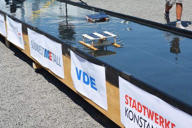 In einem langen Wasserbecken schwimmen zwei Modellboote mit Solarzellen auf dem Dach.