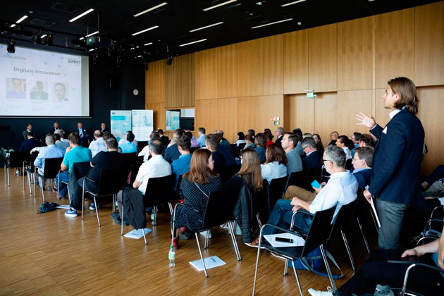 Ein Präsentationssaal voller Zuschauer. Ein Mann steht inmitten der Zuschauerreihen und spricht. Vorne steht auf einer Leinwand "Digitale Innovation".