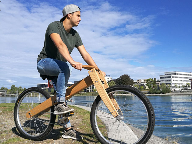 Ein junger Mann sitzt auf einem Fahrrad mit Holzrahmen.