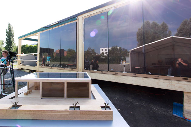 Das Modell eines modularen Solarhauses steht vor einer großen Fensterwand des Solarhauses, das das Modell zeigt.