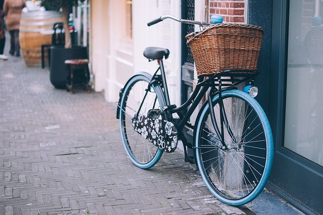 Ein hellblaues Fahrrad mit einem geflochtenen Korb am Lenker lehnt an einer Hauswand.