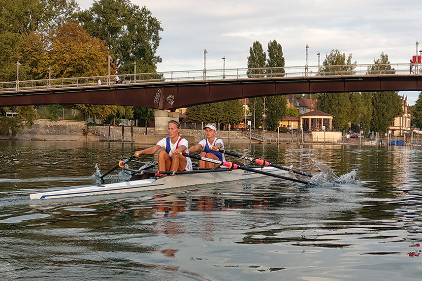Zwei Frauen in einem Ruderboot unterqueren auf dem Konstanzer Seerhein die Fahrradbrücke.