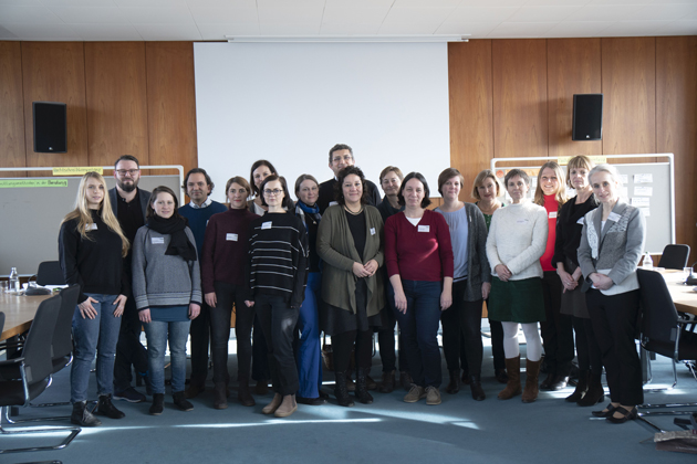 Die Veranstaltungsteilnehmer stehen in einer Gruppe im Senatssaal der Hochschule und blicken in Richtung der Fotografin.