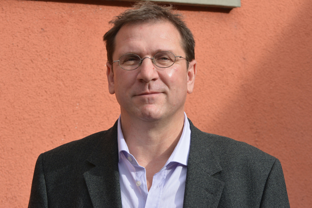 Prof. Dr. Thomas Göllinger im Portrait vor einer orange-roten Wand.