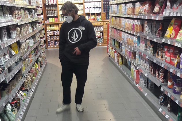 Ein junger Mann steht zwischen zwei Regalen im Supermarkt. Er trägt eine Eye-tracking-Brille und blickt auf die Auslage im linken Regal.
